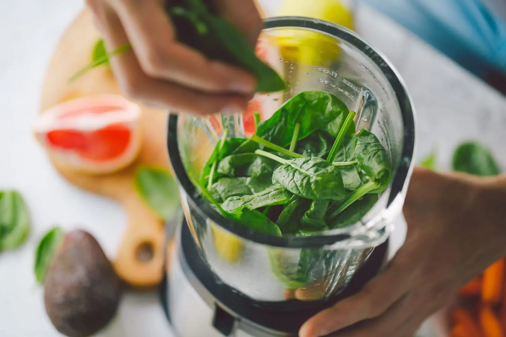 A person is holding a blender with spinach in it.